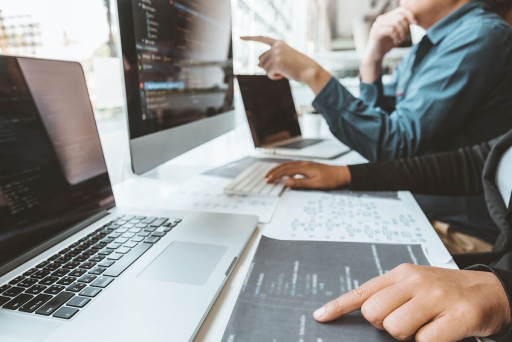 Two web developers discussing web development code on multiple computer screens