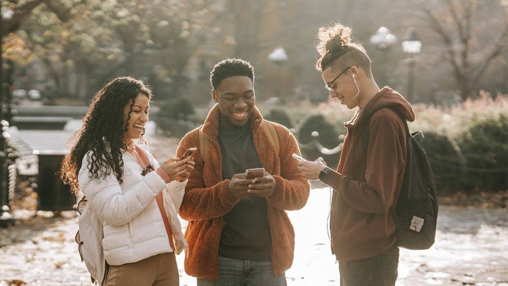 Three friends smiling looking at their phones