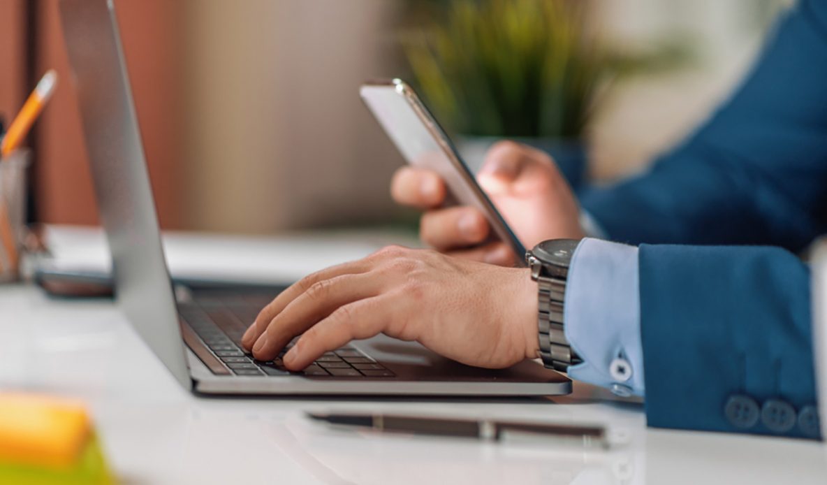 hand holding phone and hand working on laptop