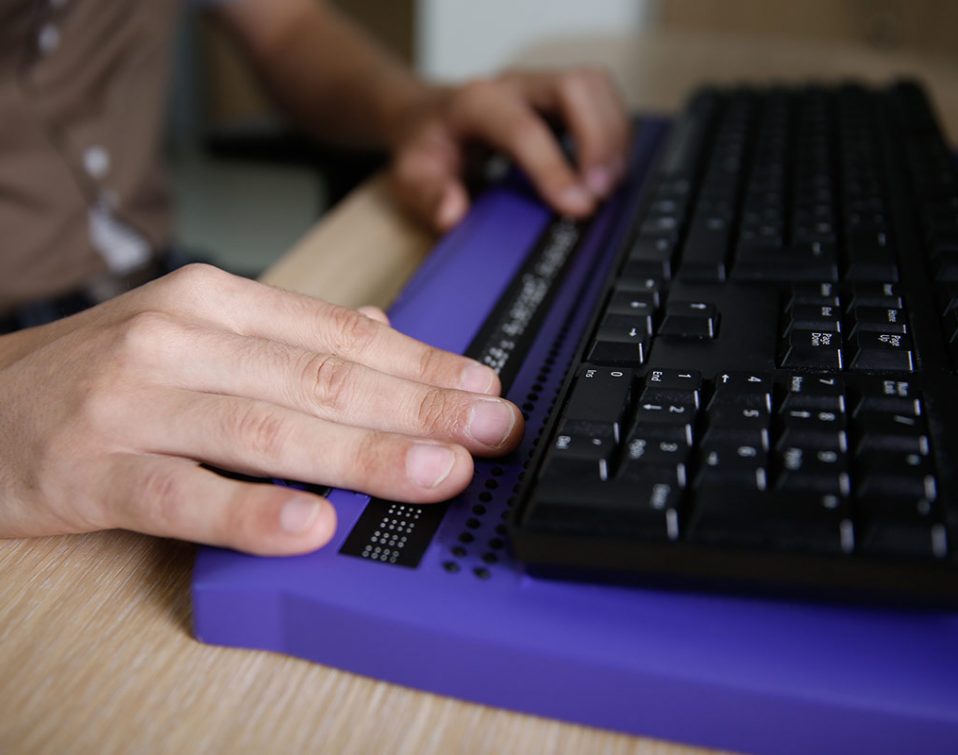 Person browsing the internet with a keyboard that has a braille attachement