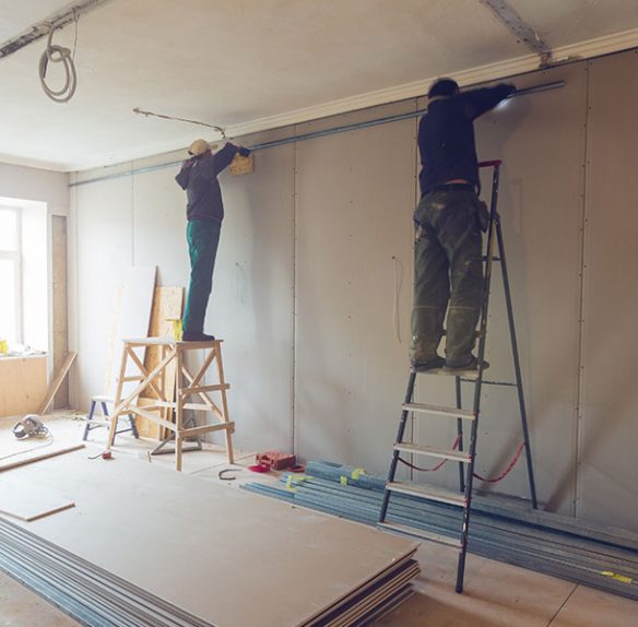 Two men installing drywall in a room