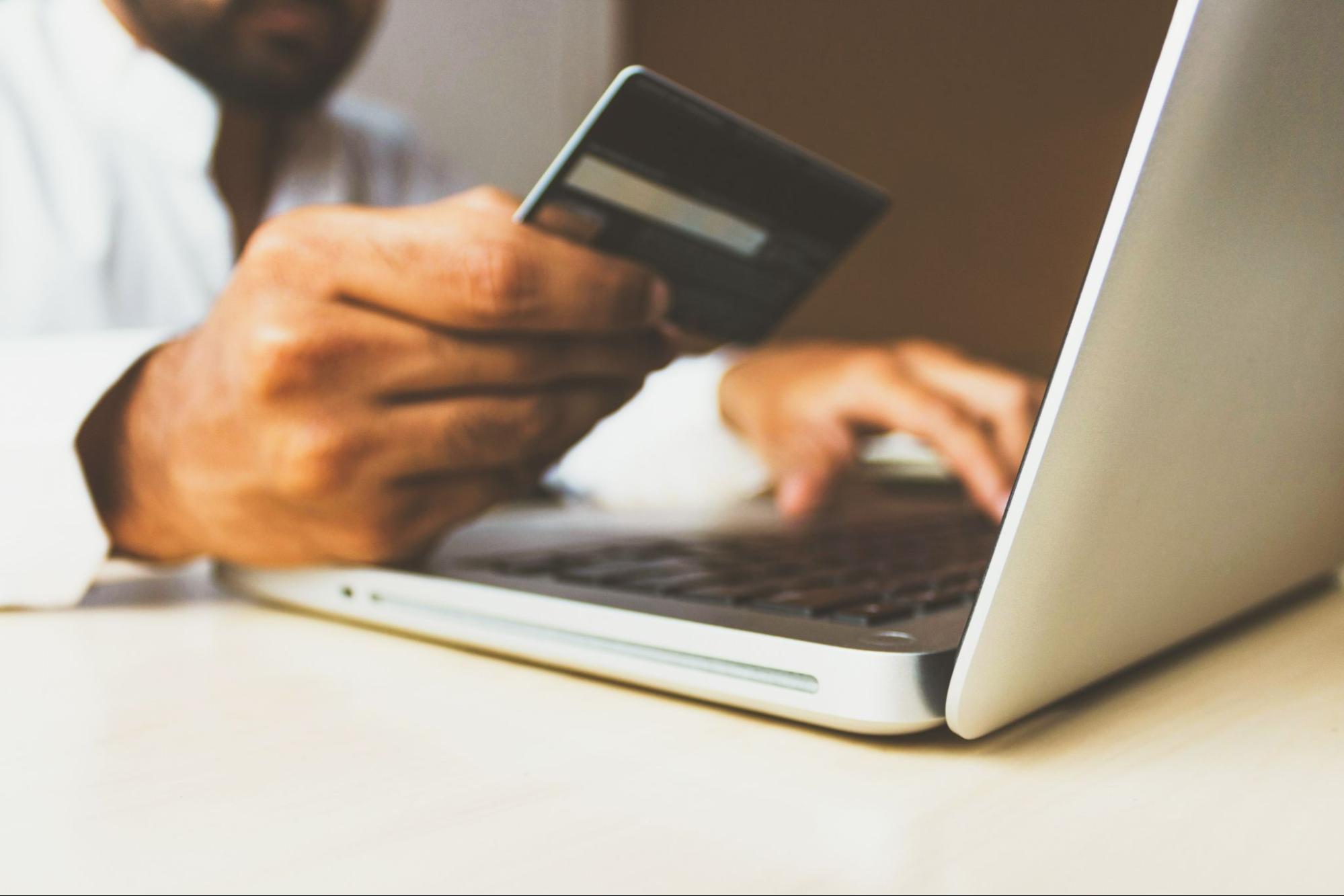 man-holding-credit-card-to-pay-with-laptop-open