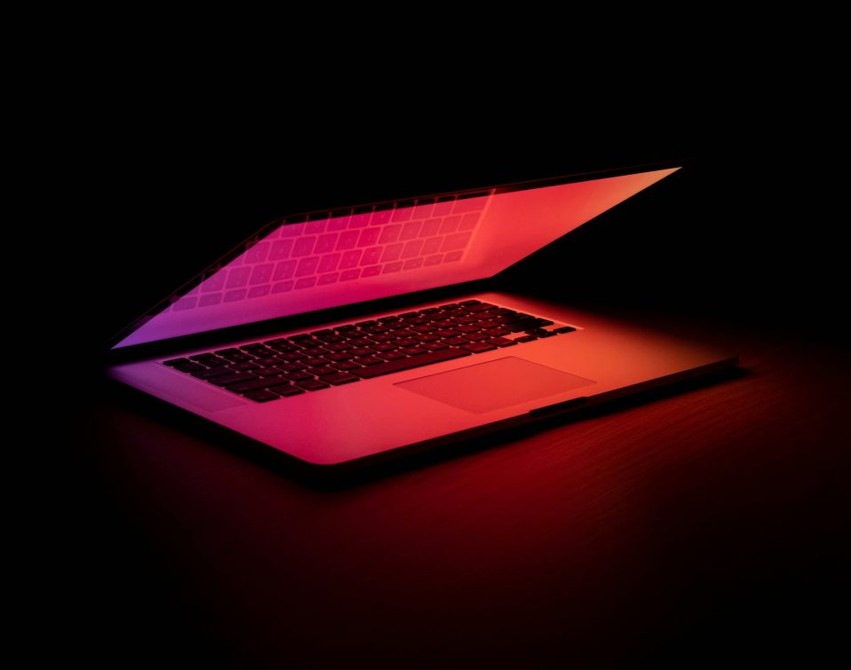Laptop glowing with red and pink light against a dark background.